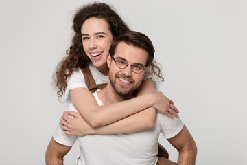 Young man in eyeglasses giving piggyback ride to happy attractive woman.