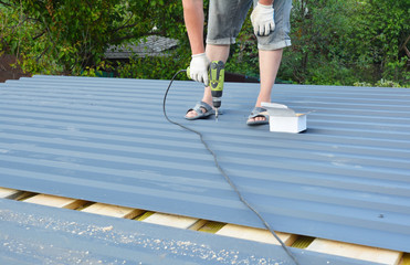 Roofer with screw gun installing  corotile lightweight metal roofing sheets roofing  construction