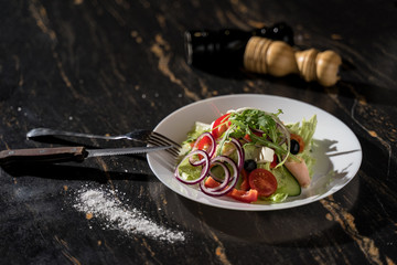greek salad with cheese tomatoes onions greens and cucumbers in a large plate with the addition on a dark background