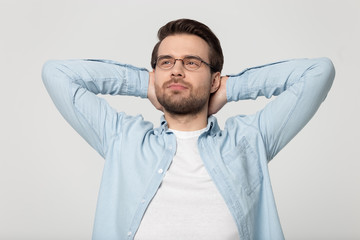 Peaceful young man in eyeglasses folding hands behind head, relaxing.