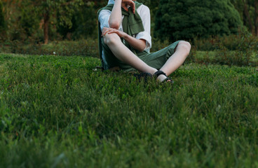 boy in a white shirt, green shorts and a sweater sits on green grass