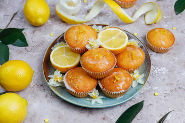 Delicious freshly baked homemade lemon muffins with lemons on a plate on light background