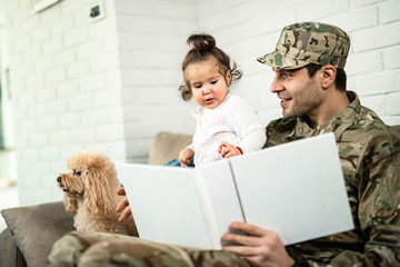 Happy military officer and his daughter looking at photo album while relaxing at home.