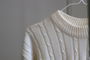 White cable knit sweater on a clothes rack. Selective focus.