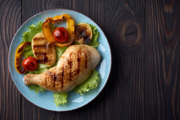 Grilled chicken leg with vegetables on a blue plate