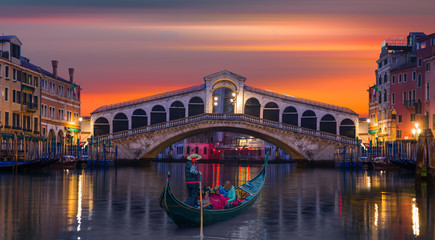 Gondolier carries tourists on gondola Green Canal near Rialto Bridge at sunset - Venice, Italy