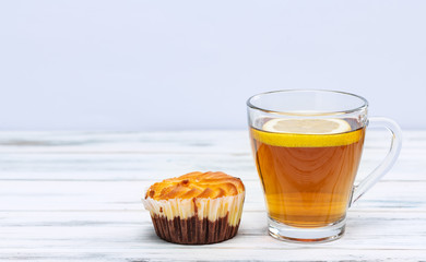 Cup of hot tea with lemon and cookies on a white wooden background.