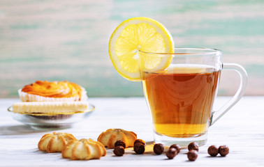 Cup of hot tea with lemon and cookies on a white wooden background.