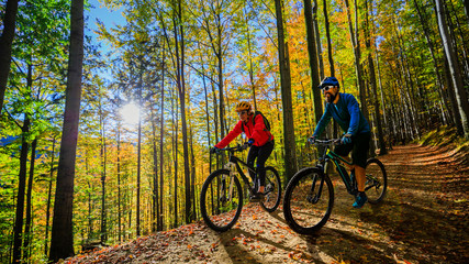 Cycling woman and men riding on bikes at sunset mountains forest landscape. Couple cycling MTB...