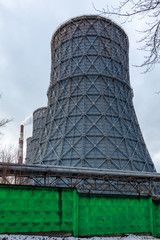 Three huge metal pipes of a thermal power plant fenced by a green concrete fence