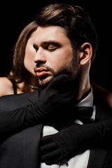 young woman in gloves touching bearded man isolated on black