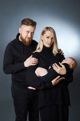 Man and a woman hold a baby in their arms. Portrait of a married couple after the birth of a child. Young family