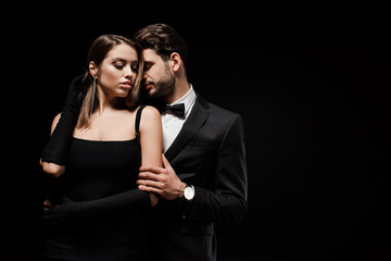 handsome man in suit hugging attractive woman in gloves isolated on black