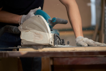 Carpenter man in white gloves works on jigsaw
