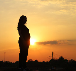 Pregnant woman silhouette standing in the sunset.