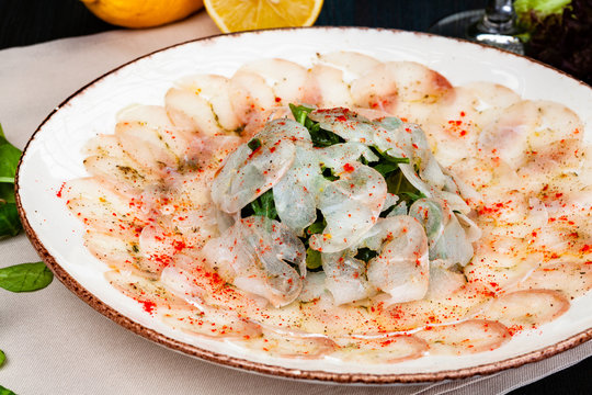 Dorado fish carpaccio served with arugula salad on white plate.