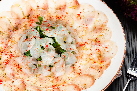 Dorado fish carpaccio served with arugula salad on white plate.