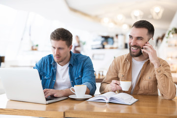 two successful colleagues men solving work issues during coffee break at cafe, working in their laptops on common business project , multitasking and teamwork concept