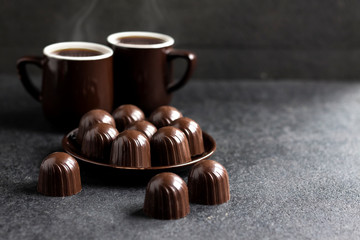 Chocolate candies on a plate and two cups of coffee on black background