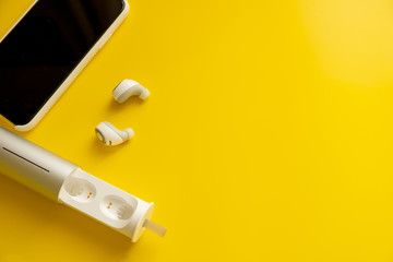Smartphone white wireless headphones on a bright yellow background, minimalism concept