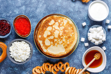 Shrovetide Maslenitsa festival meal. Russian pancake blini with raspberry jam, honey, fresh cream and red caviar,sugar cubes,cottage cheese,bubliks on dark background