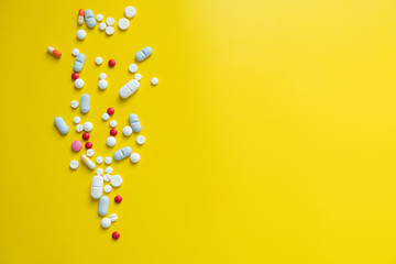 Many different colored tablets pills bright yellow background. Health and medicine concept, copyspace