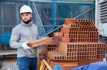 Bricklayer taking red bricks from stack