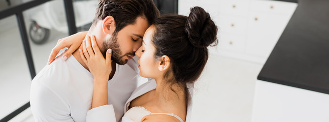Panoramic shot of girl in bra and shirt kissing boyfriend at home