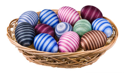 Striped hand-decorated Easter eggs in wicker basket isolated on white background. Colored empty eggshells wrapped by pasted cotton sewing thread. Traditional holiday decoration from ornate egg shells.