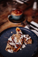 Shrove Tuesday, Pancake Day. Delicious pancakes served with fresh bananas, chocolate sauce and nuts. Cup of coffee in the background. Concept of English traditions and food. .