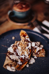 Shrove Tuesday, Pancake Day. Delicious pancakes served with fresh bananas, chocolate sauce and nuts. Cup of coffee in the background. Concept of English traditions and food. .