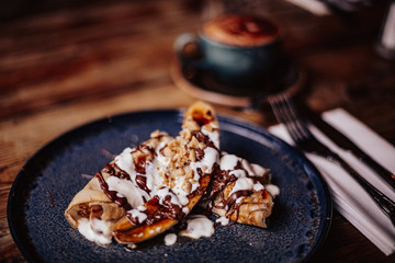 Shrove Tuesday, Pancake Day. Delicious pancakes served with fresh bananas, chocolate sauce and nuts. Cup of coffee in the background. Concept of English traditions and food. .