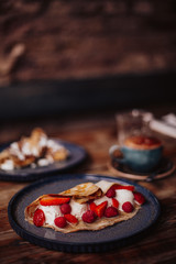 Shrove Tuesday, Pancake Day. Delicious pancakes served with fresh strawberries, vanilla ice cream and icing sugar. Cup of coffee in the background. Concept of English traditions and food.