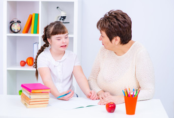 A girl with down syndrome draws at home next to the teacher.