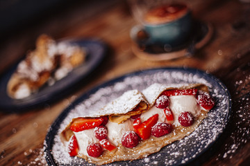 Shrove Tuesday, Pancake Day. Delicious pancakes served with fresh strawberries, vanilla ice cream and icing sugar. Cup of coffee in the background. Concept of English traditions and food.