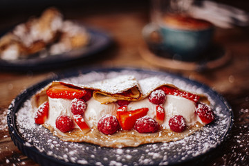 Shrove Tuesday, Pancake Day. Delicious pancakes served with fresh strawberries, vanilla ice cream and icing sugar. Cup of coffee in the background. Concept of English traditions and food.
