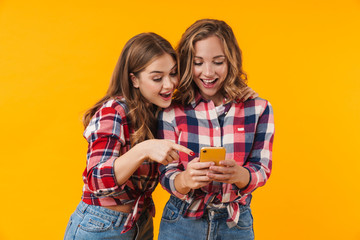 Image of two young beautiful girls smiling and using cellphone