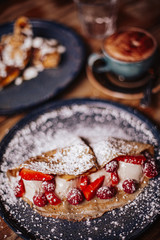 Shrove Tuesday, Pancake Day. Delicious pancakes served with fresh strawberries, vanilla ice cream and icing sugar. Cup of coffee in the background. Concept of English traditions and food.
