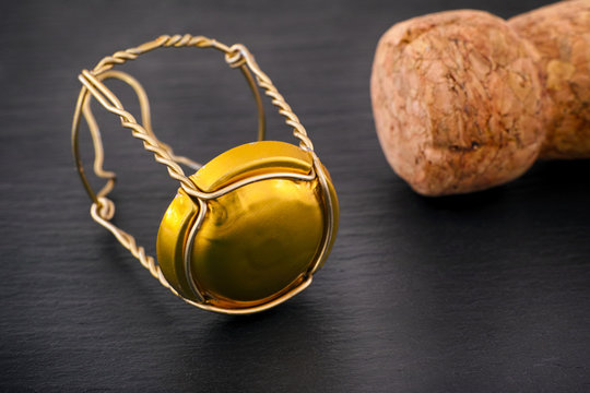 Champagne muselet with gold cap and cork on black stone background.