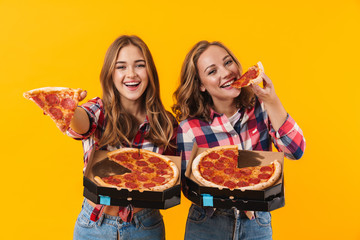 Image of two young beautiful girls wearing plaid shirts eating pizza