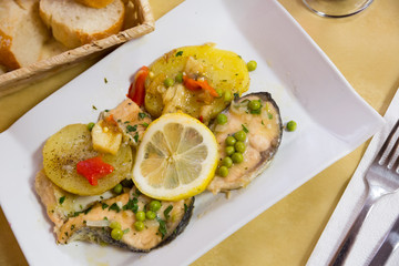 Delicious fried salmon fillets served with lemon, potato, bell peppers and greens peas