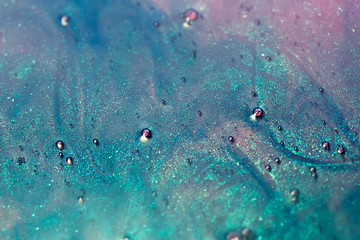 Fototapeta na wymiar macro shot of blue and pink alcohol ink with glitter dissolving in water, abstract background