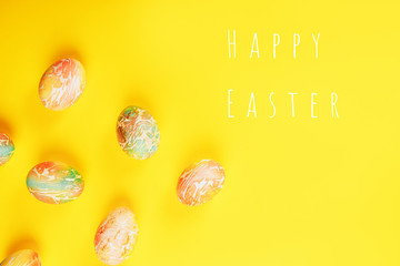 Easter eggs painted in orange and green colors on yellow background, flat lay, space for text