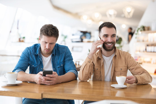 two handsome colleagues men out of office during coffee break at cafe, drinking coffee, checking news in their smartphones , speaking on the phone, multitasking concept