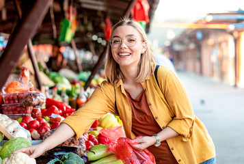 Portrait of young woman standing in front of a vegetable counter in an outdoor market.