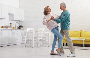 Obraz premium Happy senior couple dancing together in kitchen