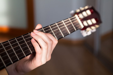 Acoustic guitar fretboard with female long fingers hand striking a chord