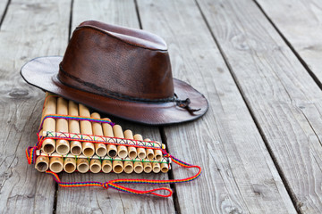 Multiple pipes pan flute and leather cowboy brown hat lying on square-edged flooring, copy space