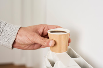 man putting a cup of coffe on a radiator