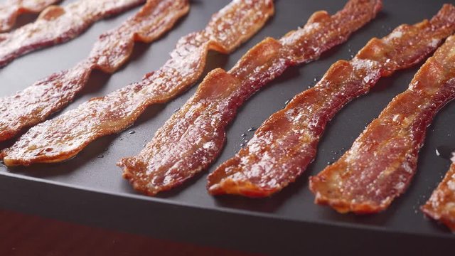 Delicious crispy bacon strips cooking on a flat top grill.